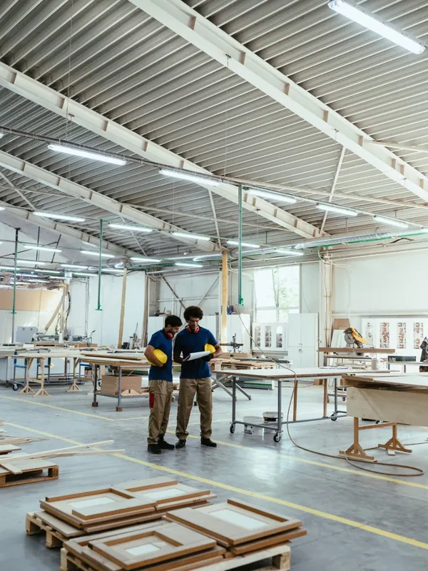 Deux artisans menuisiers consultant un plan dans un atelier industriel lumineux